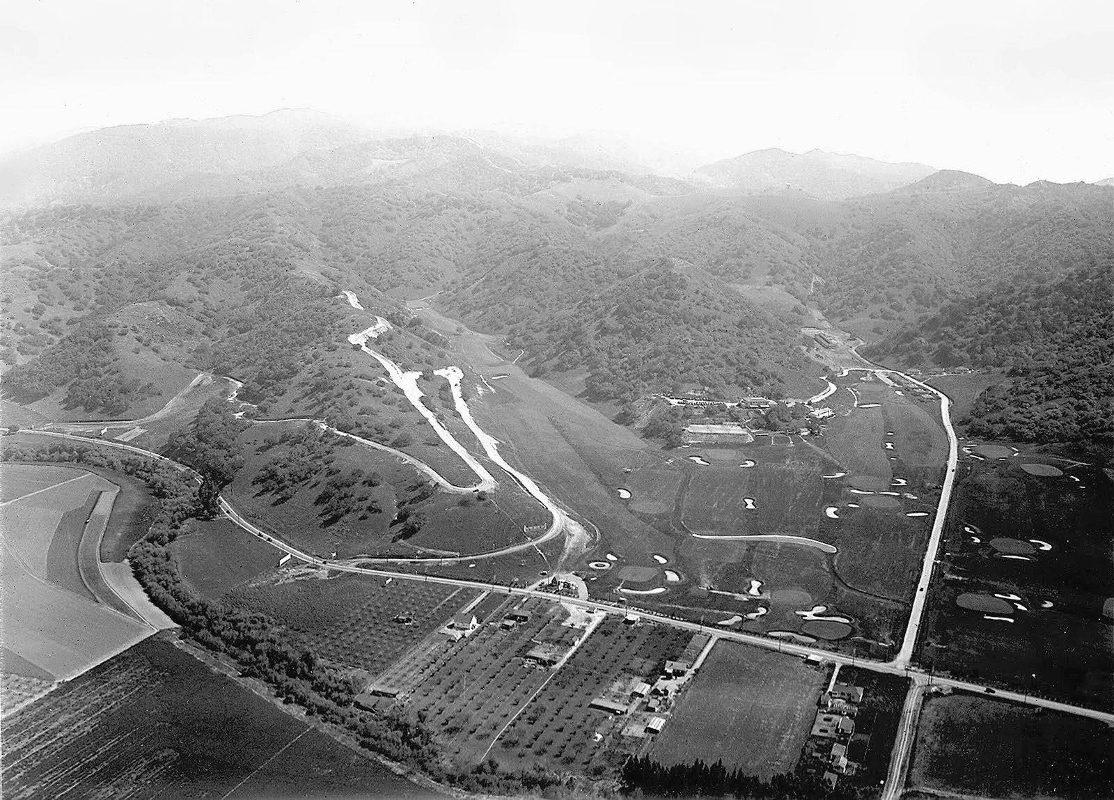 Vista aérea de un club de campo con calles de golf sinuosas rodeadas de una ladera boscosa